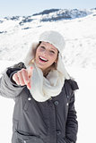 Woman in warm clothing pointing at camera on snow covered landscape