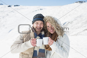 Cheerful couple in warm clothing with coffee cups on snowed landscape