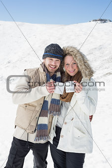 Couple in warm clothing with coffee cups on snowed landscape