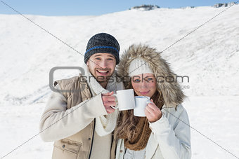 Couple in warm clothing with coffee cups on snowed landscape