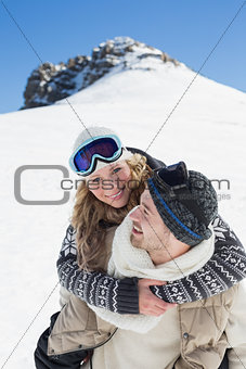 Man piggybacking cheerful woman against snowed hill