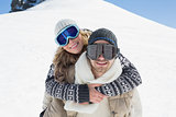 Man piggybacking woman in ski goggles against snow