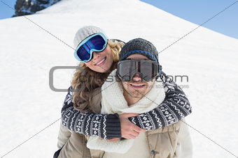 Man piggybacking woman in ski goggles against snow