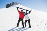 Full length of a cheerful couple with ski board on snow