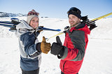 Smiling couple with ski boards gesturing thumbs up on snow