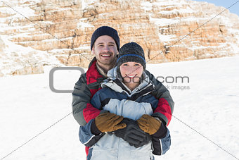Portrait of a happy man embracing woman from behind on snow
