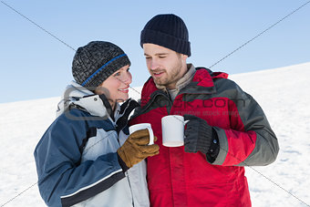 Couple in warm clothing with coffee cups on snow