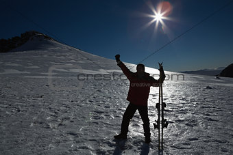 Silhouette man raising hand with ski board on snow