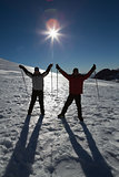 Silhouette couple raising hands with ski poles on snow