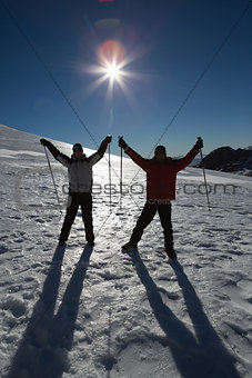 Silhouette couple raising hands with ski poles on snow
