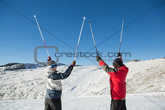Rear view portrait of a couple raising ski poles on snow