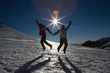 Silhouette couple jumping on snow against sun and blue sky