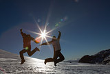 Silhouette couple jumping on snow against sun and blue sky