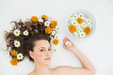 Beautiful woman lying with bowl of flowers in beauty salon