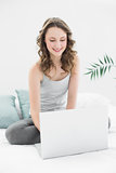 Smiling casual young brunette using laptop in bed