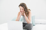 Smiling casual brunette looking at laptop in bed