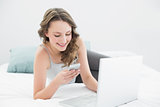 Smiling casual woman with cellphone and laptop in bed