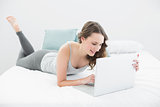 Smiling casual brunette using laptop in bed