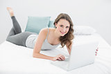 Smiling casual young brunette using laptop in bed