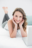 Smiling casual young brunette with laptop in bed