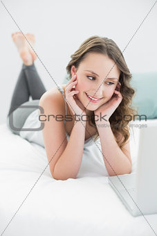 Smiling casual brunette with laptop in bed