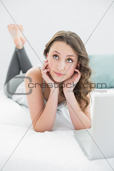 Thoughtful casual brunette with laptop in bed