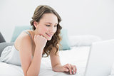 Smiling casual brunette using laptop in bed