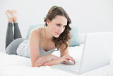 Relaxed casual brunette using laptop in bed