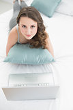 Casual young brunette with laptop lying in bed