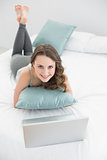Casual brunette with laptop lying in bed