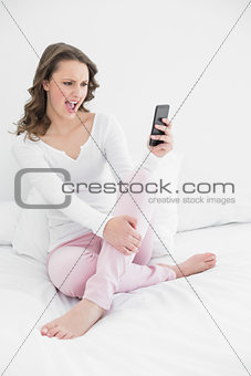 Cheerful woman looking at mobile phone in bed