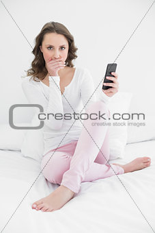 Shocked woman with mobile phone in bed