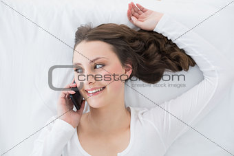 Young brunette using mobile phone in bed
