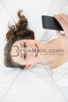 Young brunette with mobile phone in bed