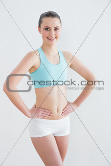 Smiling toned woman with hands on hips against wall