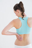Rear view of a toned woman with back pain against wall