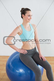 Smiling fit woman on exercise ball in fitness studio
