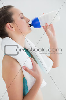 Woman with dumbbells drinking water against wall