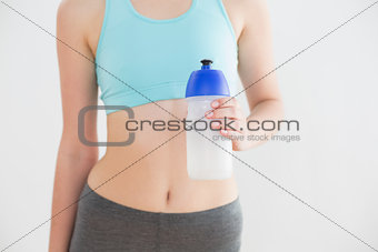Mid section of fit woman holding water bottle against wall