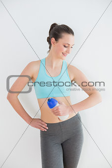 Toned young woman holding water bottle against wall