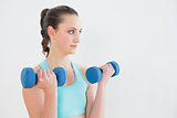 Serious woman with dumbbells against wall