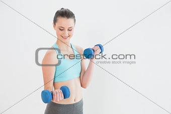 Smiling woman with dumbbells against wall