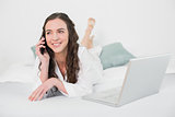 Casual woman using cellphone and laptop in bed