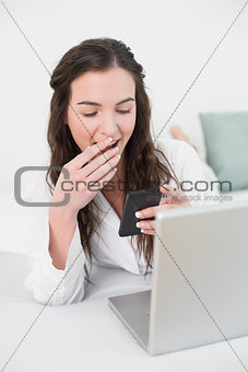 Shocked smiling woman looks at mobile phone in bed