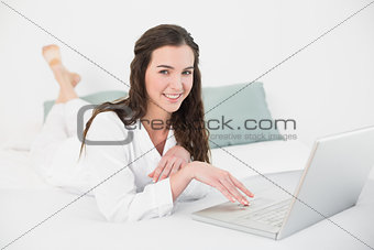 Relaxed smiling casual brunette using laptop in bed