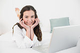 Relaxed smiling casual brunette with laptop in bed