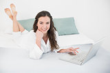 Relaxed smiling casual brunette with laptop in bed