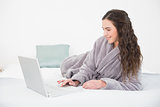 Brunette in bathrobe using laptop in bed