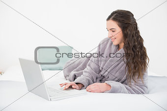 Brunette in bathrobe using laptop in bed