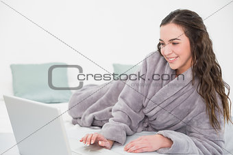 Relaxed brunette in bathrobe using laptop in bed